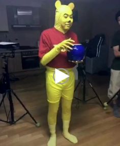 a man dressed as winnie the pooh holding a blue bowl in front of him