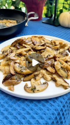 a white plate topped with sliced mushrooms on top of a blue table cloth next to a skillet