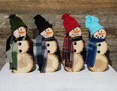 four snowmen are lined up next to each other in hats and scarves on wood slices