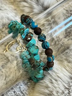 Turquoise chips with a toggle clasp. The other bracelet has turquoise and black swirls with hits of light yellow with brown wood beads. Rustic Adjustable Turquoise Beaded Bracelets, Adjustable Turquoise Beaded Bracelets With Wooden Beads, Rustic Blue Adjustable Beaded Bracelet, Rustic Blue Adjustable Beaded Bracelets, Rustic Adjustable Blue Beaded Bracelet, Rustic Handmade Blue Beaded Bracelets, Adjustable Turquoise Bracelets With Wooden Beads, Bohemian Turquoise Bracelets With Wooden Beads, Rustic Turquoise Beaded Bracelets With Natural Stones