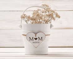 a small white bucket filled with flowers on top of a wooden table