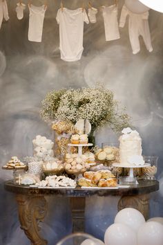 a table topped with lots of desserts next to white balloons and bundts