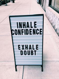 an inhale and exhale sign sitting on the side of a sidewalk next to a building