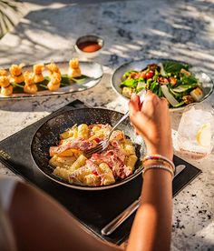 a woman is eating some food on the table with other plates and bowls in front of her