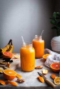 two jars filled with orange juice sitting on top of a table next to sliced fruit