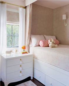 a white bed sitting under a window next to a dresser with a stuffed animal on top of it