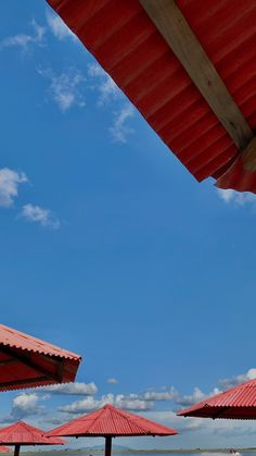 several red umbrellas sitting on the beach under a blue sky with clouds in the background