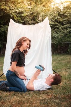 a pregnant woman sitting on the ground next to a man holding a hair dryer