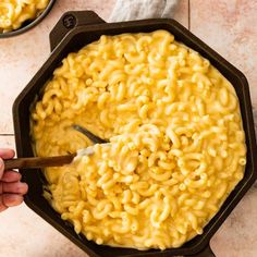 someone is stirring macaroni and cheese in a skillet