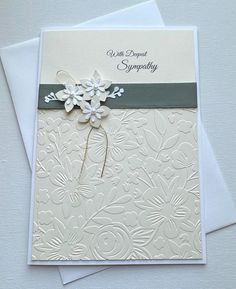 a white card with flowers on it and a green ribbon around the edge, sitting on top of two cards