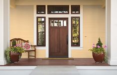 two potted plants sit on the front porch of a house with yellow siding and brown doors