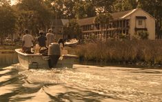 several people are riding in a small boat on the water near some houses and trees