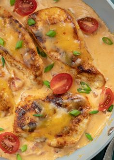 a pan filled with chicken covered in cheese and tomato slices, garnished with green onions