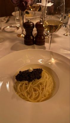 a white plate topped with pasta and sauce next to glasses of wine on a table