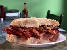 a bacon sandwich on a white plate sitting on a table