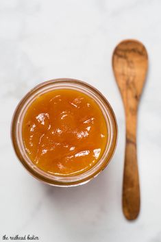 a wooden spoon sitting next to a glass jar filled with orange marmalade sauce