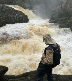 a man with a backpack is standing in front of a waterfall and looking at his cell phone