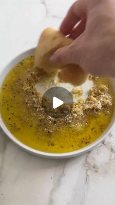 a person dipping something into a bowl with mustard and seasoning in it on a marble counter top