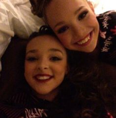 two women laying next to each other on top of a bed together smiling at the camera