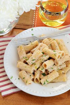 a white plate topped with pasta on top of a wooden table next to a cup of tea