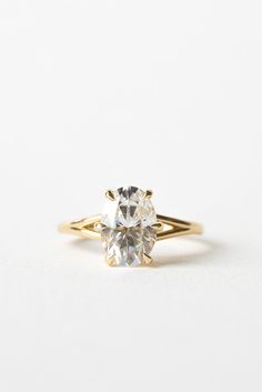 a yellow gold engagement ring with an oval cut diamond in the center, on a white background