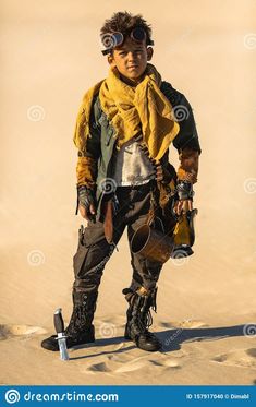 a young man dressed in steam punk clothing and goggles standing on the sand dunes