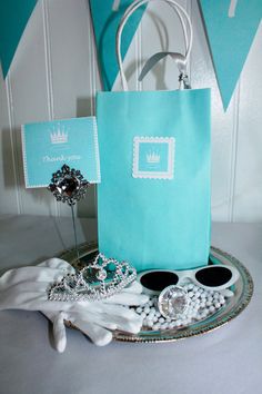 a blue paper bag sitting on top of a silver platter filled with white gloves and jewelry