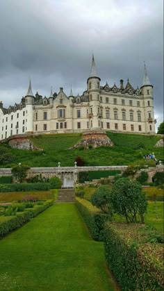 a large building with many windows sitting on top of a lush green field next to trees and bushes