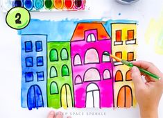 someone is painting some colorful buildings with watercolors on the paper and crayons