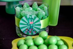 green candies are in a yellow bowl and on a table next to a cup