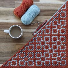 a knitted table runner next to a cup of coffee and crochet hooks