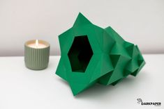 an origami candle holder next to a green paper sculpture with a lit candle