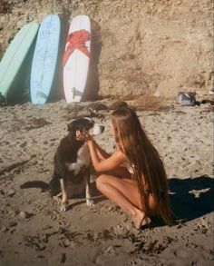 a woman sitting on the beach with her dog next to surfboards