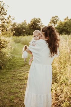 a woman holding a baby in her arms while walking through tall grass with other people