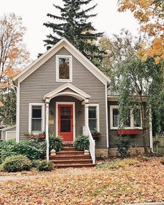 a gray house with red front door and steps leading up to the entryway is surrounded by fall foliage