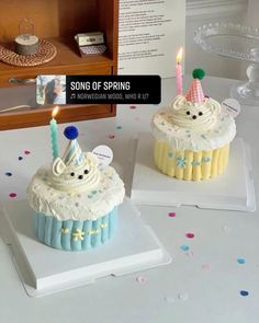 two cupcakes with candles are on display in front of a bookcase that says song of spring