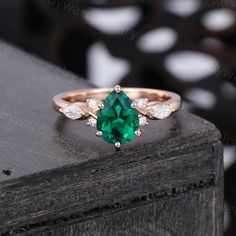 an emerald and diamond ring sitting on top of a wooden table