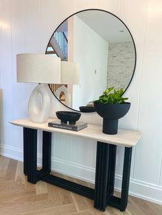 a table with a mirror, vase and lamp on it in front of a white wall