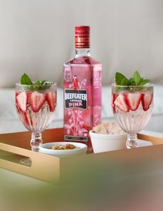 pink spritz with strawberries and mint in two glasses on a tray next to a bottle of gin