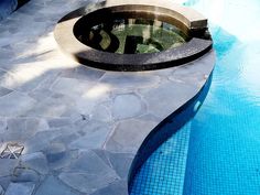 an empty swimming pool surrounded by stones and water features a circular grill in the center