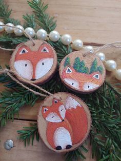 three wooden ornaments decorated with foxes and pine needles on a table next to pearls, beads and greenery