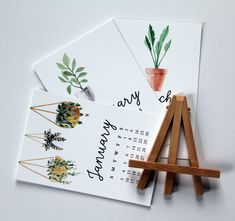 three calendars with plants on them sitting next to an easel and paintbrush