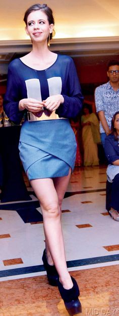 a woman is walking down the runway in a blue dress and black heels with her legs crossed