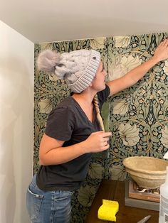 a woman in a hat is painting a wall with yellow paint and she has her hand on the mirror