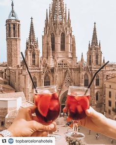 two people holding up glasses with liquid in front of a building that looks like a castle