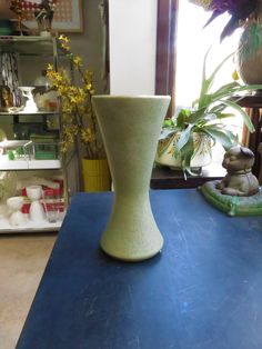 a green vase sitting on top of a blue table next to a potted plant