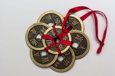 four gold coins with red ribbons tied around them on a white surface, in the shape of an ornament