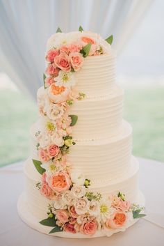 a white wedding cake with pink and orange flowers on the top tier is sitting on a table