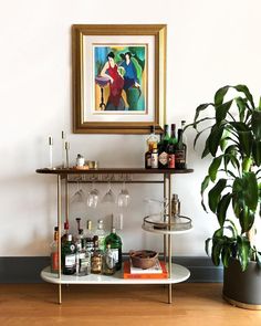 a bar cart with liquor bottles and glasses on it next to a potted plant