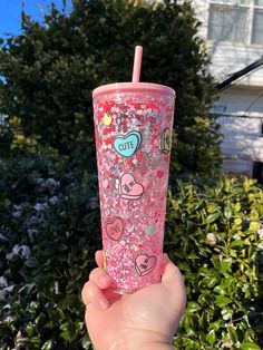 a hand holding a pink glittered cup with hearts on it and a straw in the other hand